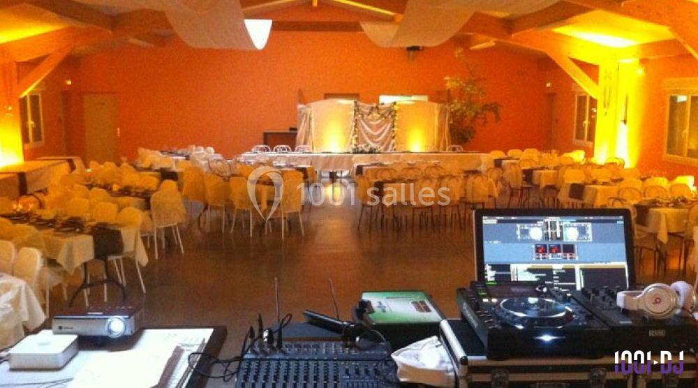 Salle de réception décorée avec des tables dressées, vue depuis une table de mixage avec matériel de DJ au premier plan.