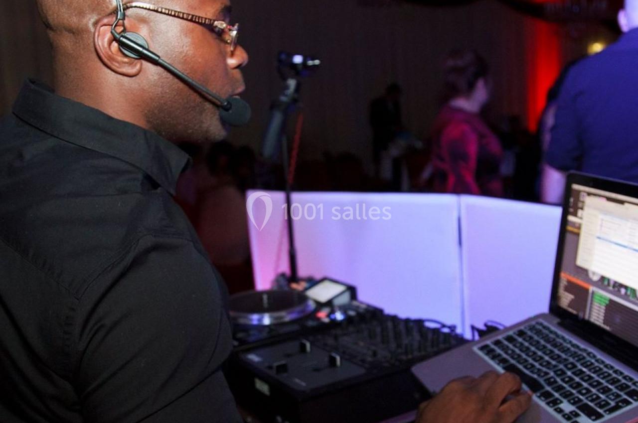 Un DJ portant un casque micro mixe de la musique sur un ordinateur portable et une table de mixage dans une salle éclairée.