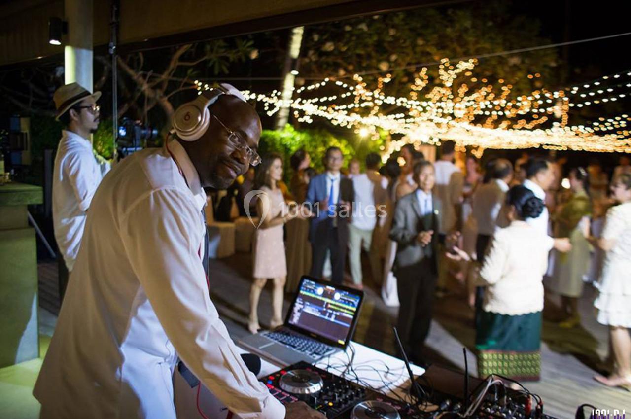 Un DJ mixe de la musique lors d'une soirée en plein air avec des invités dansant sous des guirlandes lumineuses.
