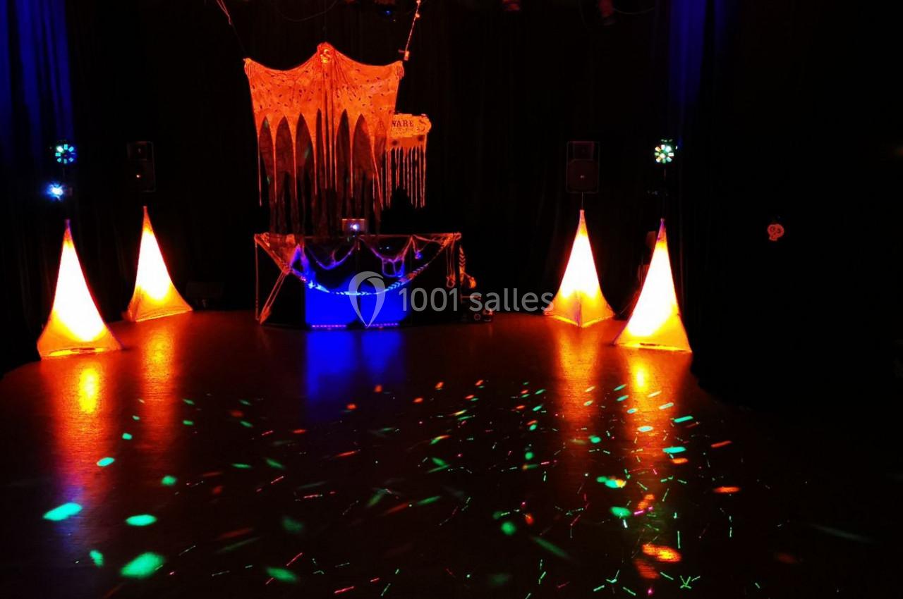 Salle sombre avec décorations lumineuses orange et bleues, piste de danse éclairée par des spots colorés.