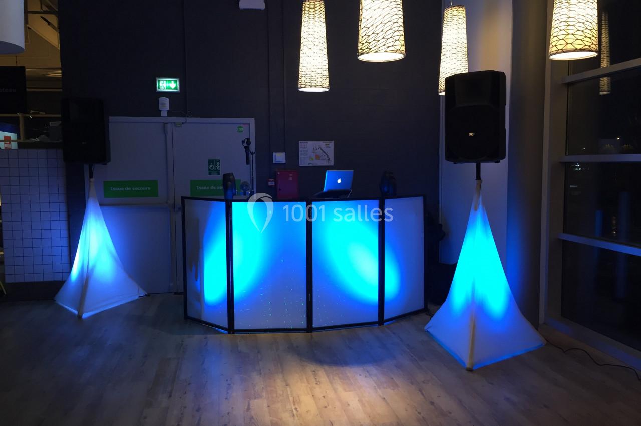 Un stand de DJ éclairé en bleu avec des enceintes et des lumières suspendues dans une salle sombre.