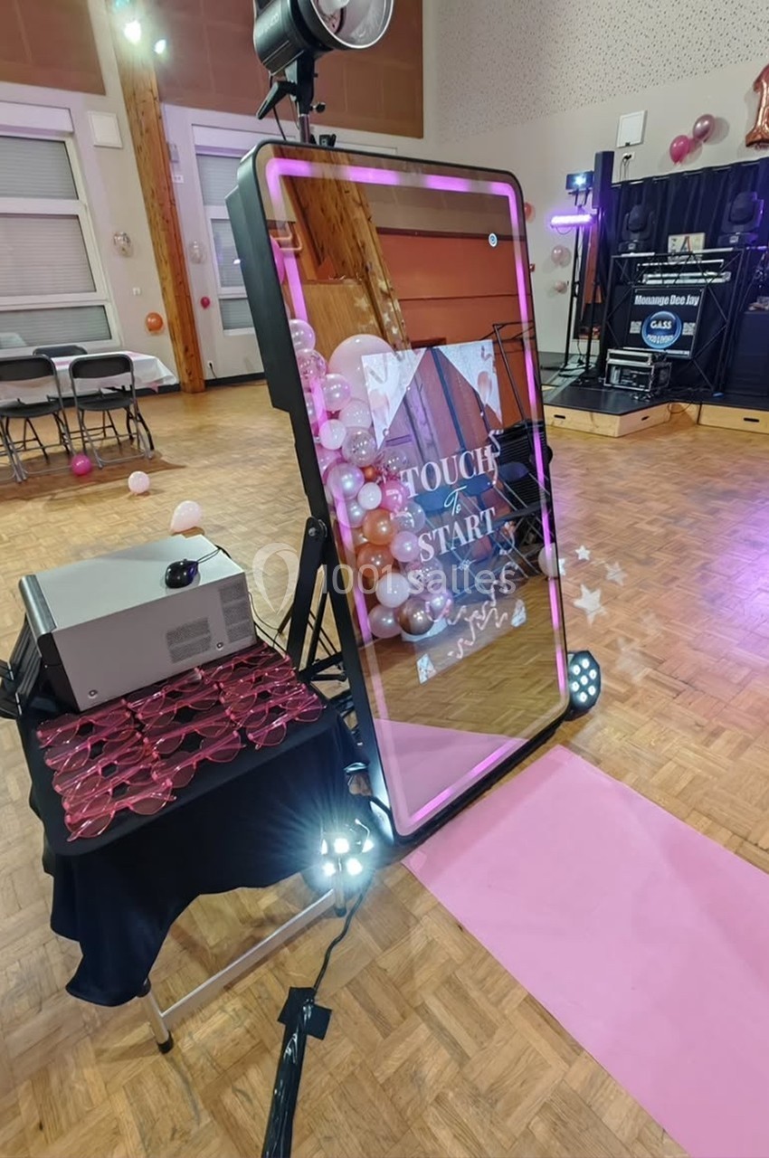 Miroir interactif avec cadre lumineux rose, installé sur un parquet, entouré de ballons et d'équipements de fête.