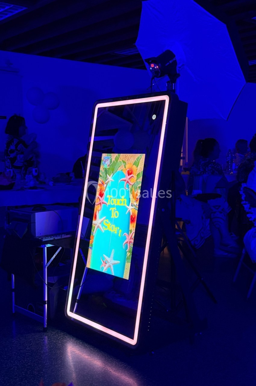 Miroir interactif lumineux dans un environnement sombre, affichant un écran tactile avec des fleurs tropicales.