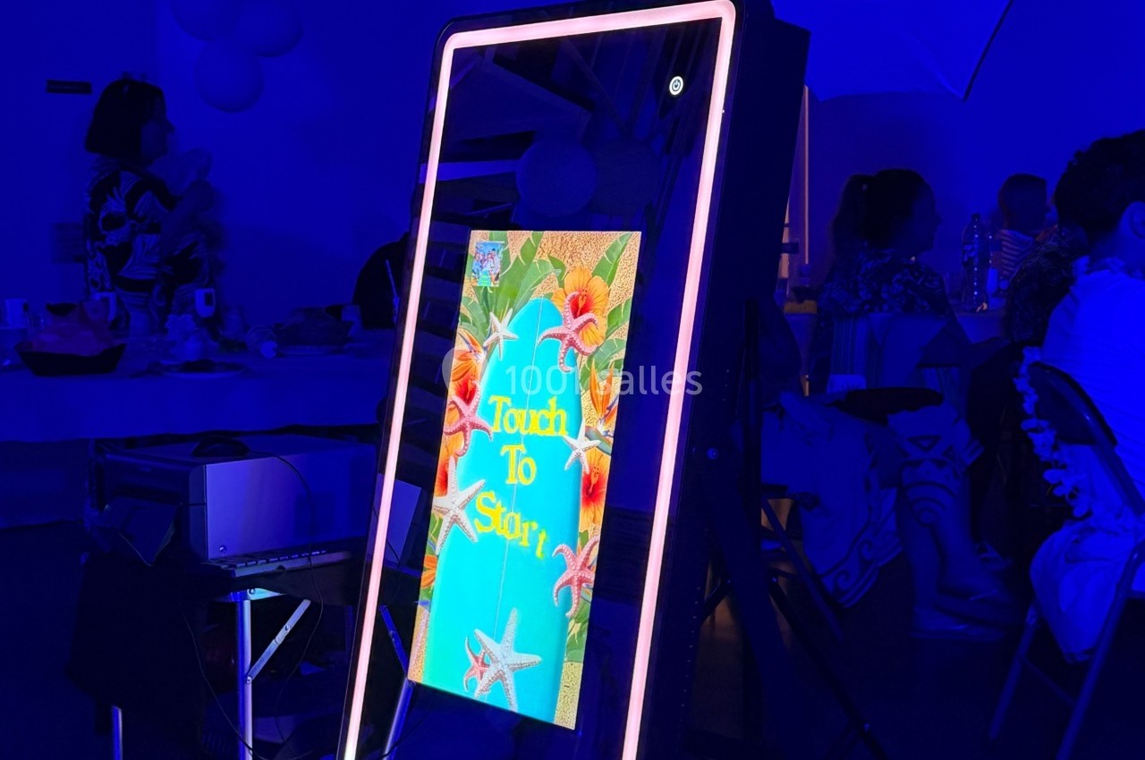 Écran interactif lumineux affichant un message ’Touch to Start’ entouré de motifs tropicaux dans un environnement sombre.