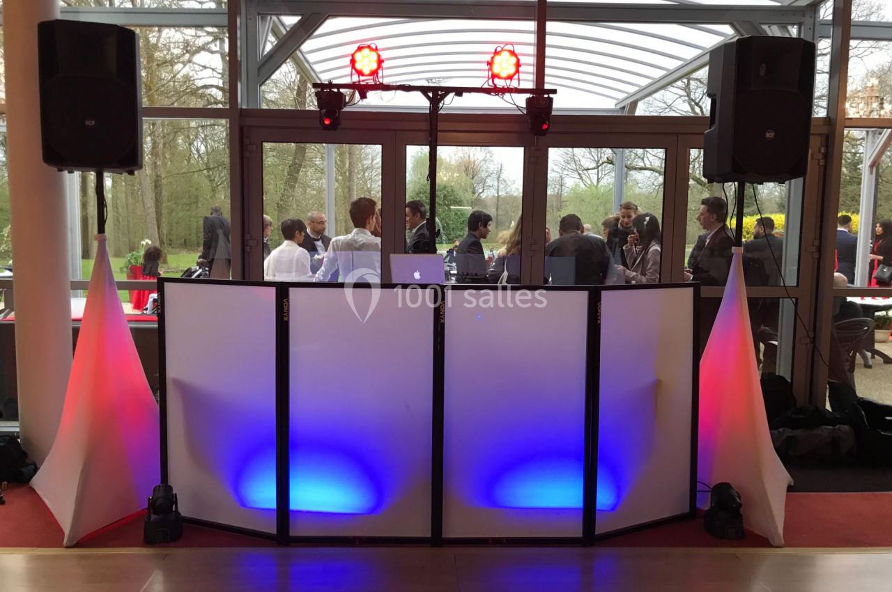 Console de DJ avec éclairage coloré devant une baie vitrée, des invités discutent en arrière-plan.