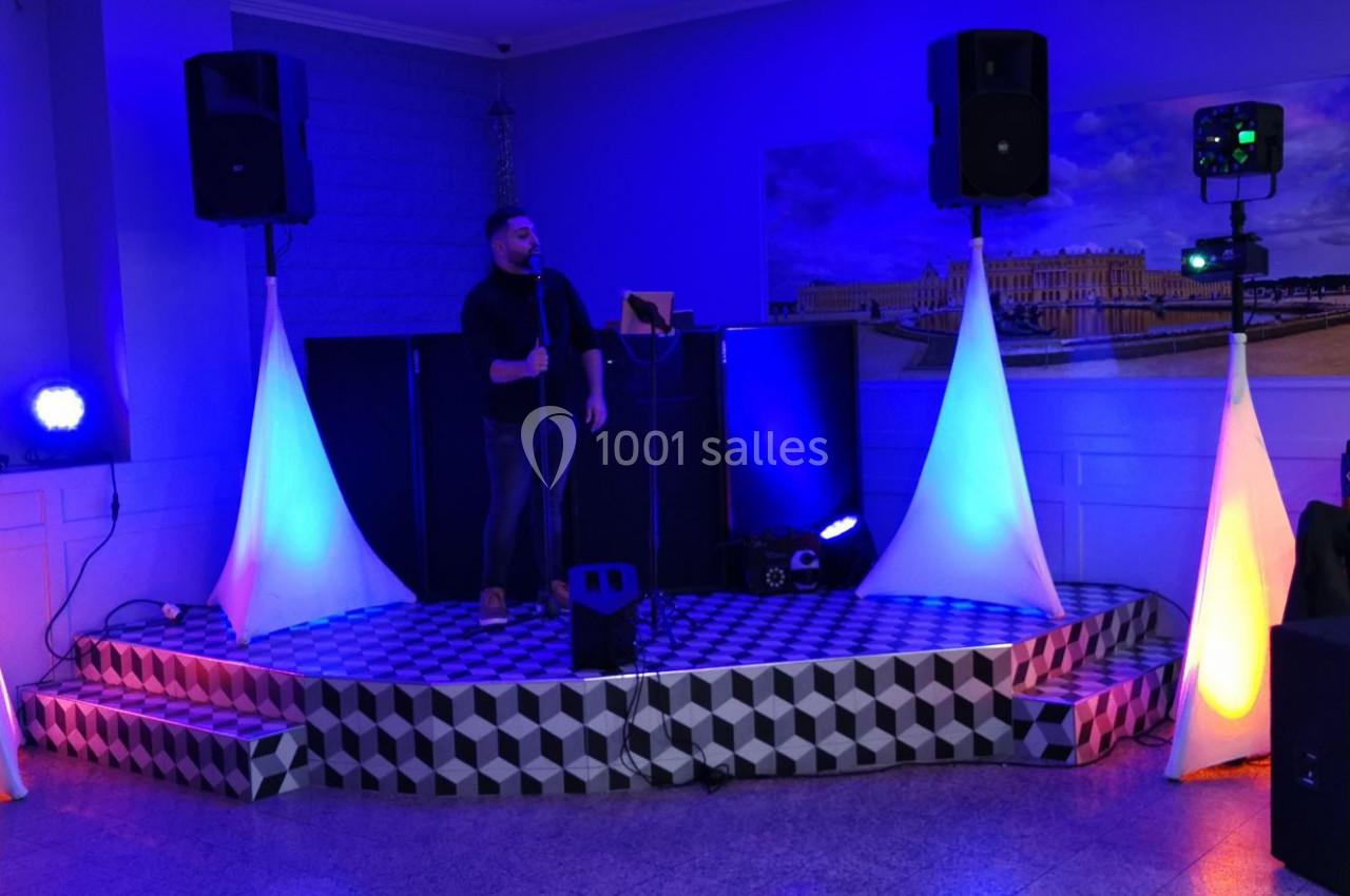 Un homme chante sur une petite scène éclairée par des lumières colorées dans une salle de réception.