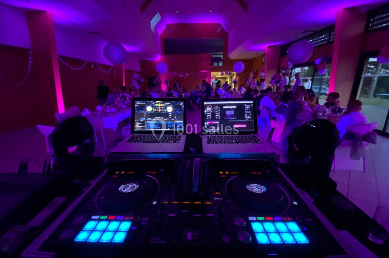 Poste de DJ avec platines et ordinateurs dans une salle de réception éclairée par des lumières violettes.