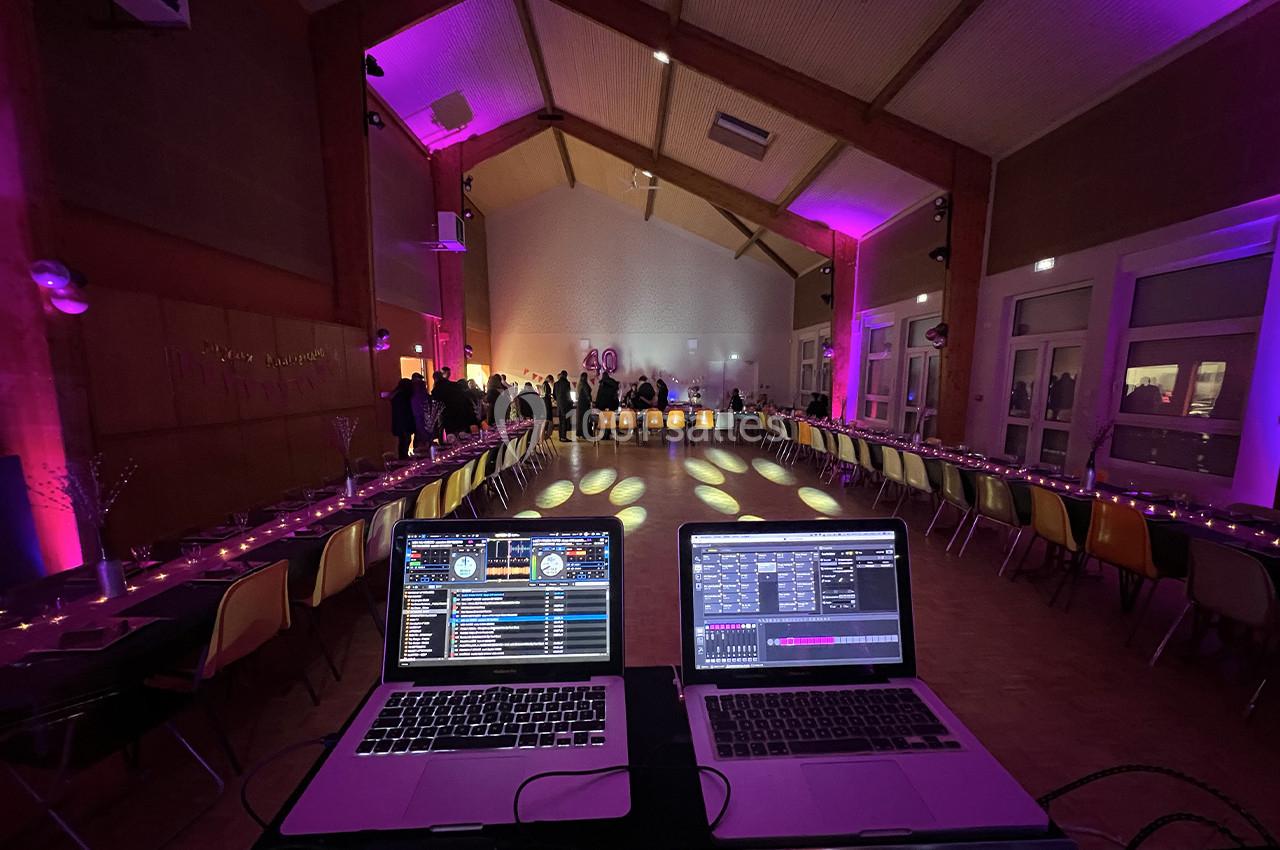 Salle de réception décorée avec des lumières colorées, vue depuis une table de mixage avec deux ordinateurs portables.