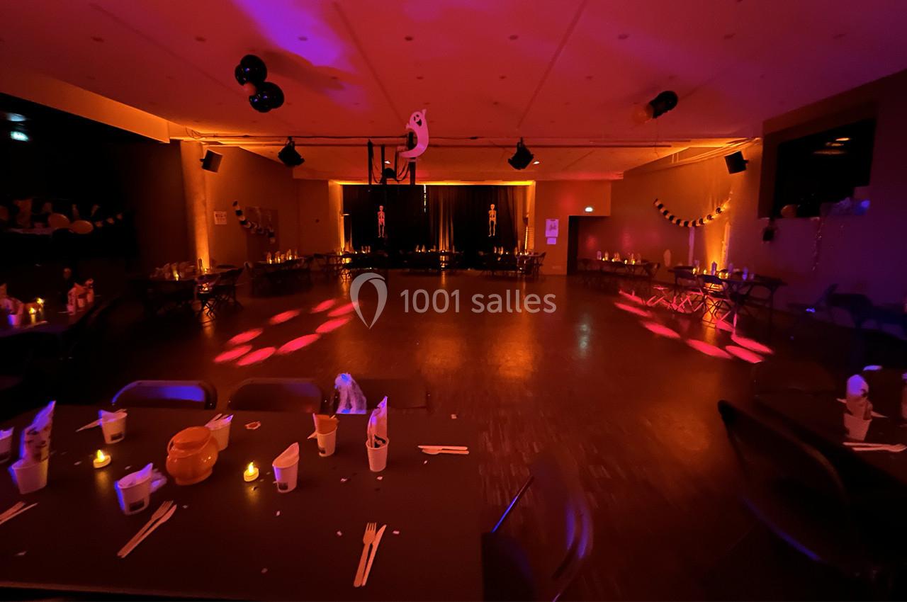 Salle décorée pour une fête, éclairée par des lumières tamisées et ornée de décorations festives sur les tables et murs.