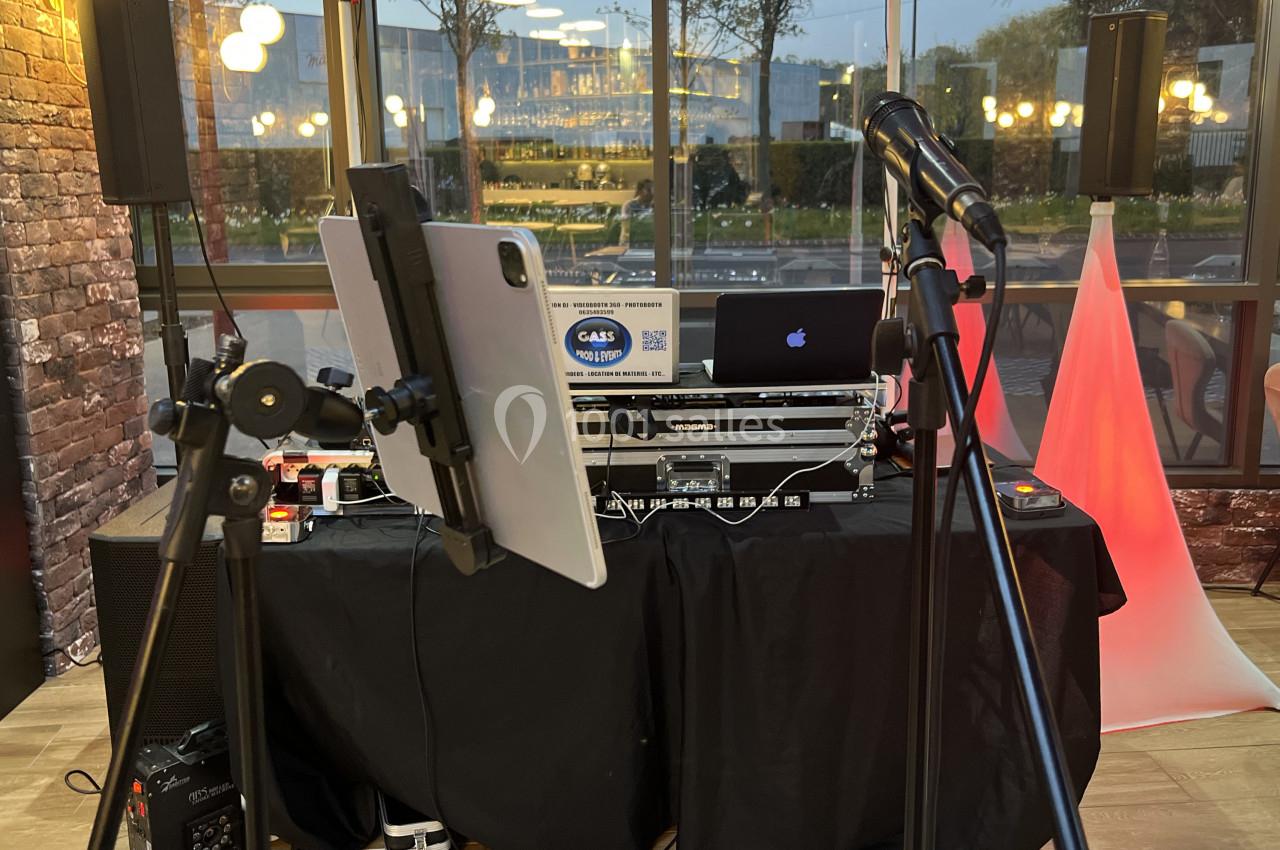 Équipement de DJ installé avec table de mixage, ordinateur, tablette et micros dans un espace intérieur vitré.