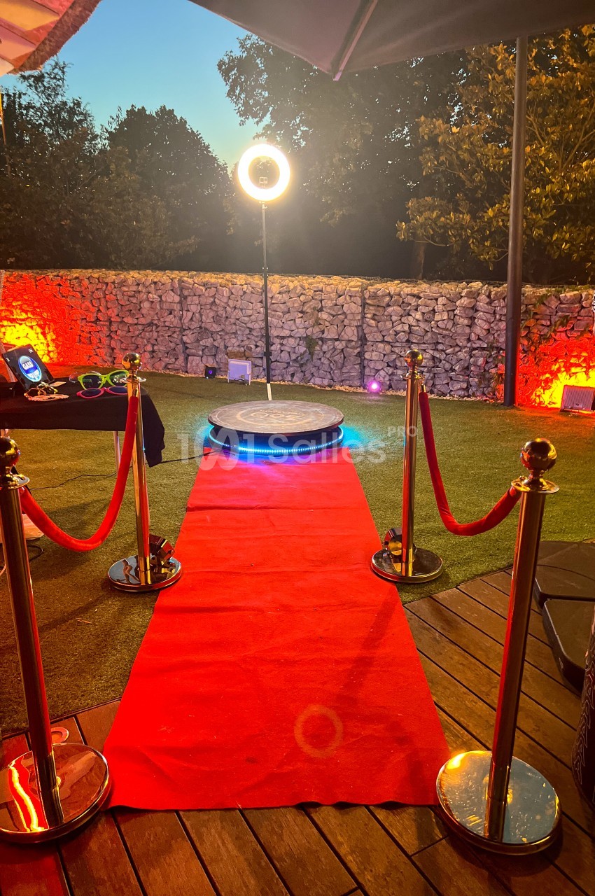 Tapis rouge menant à une plateforme circulaire éclairée, entourée de poteaux dorés et d'une lumière annulaire en extérieur.