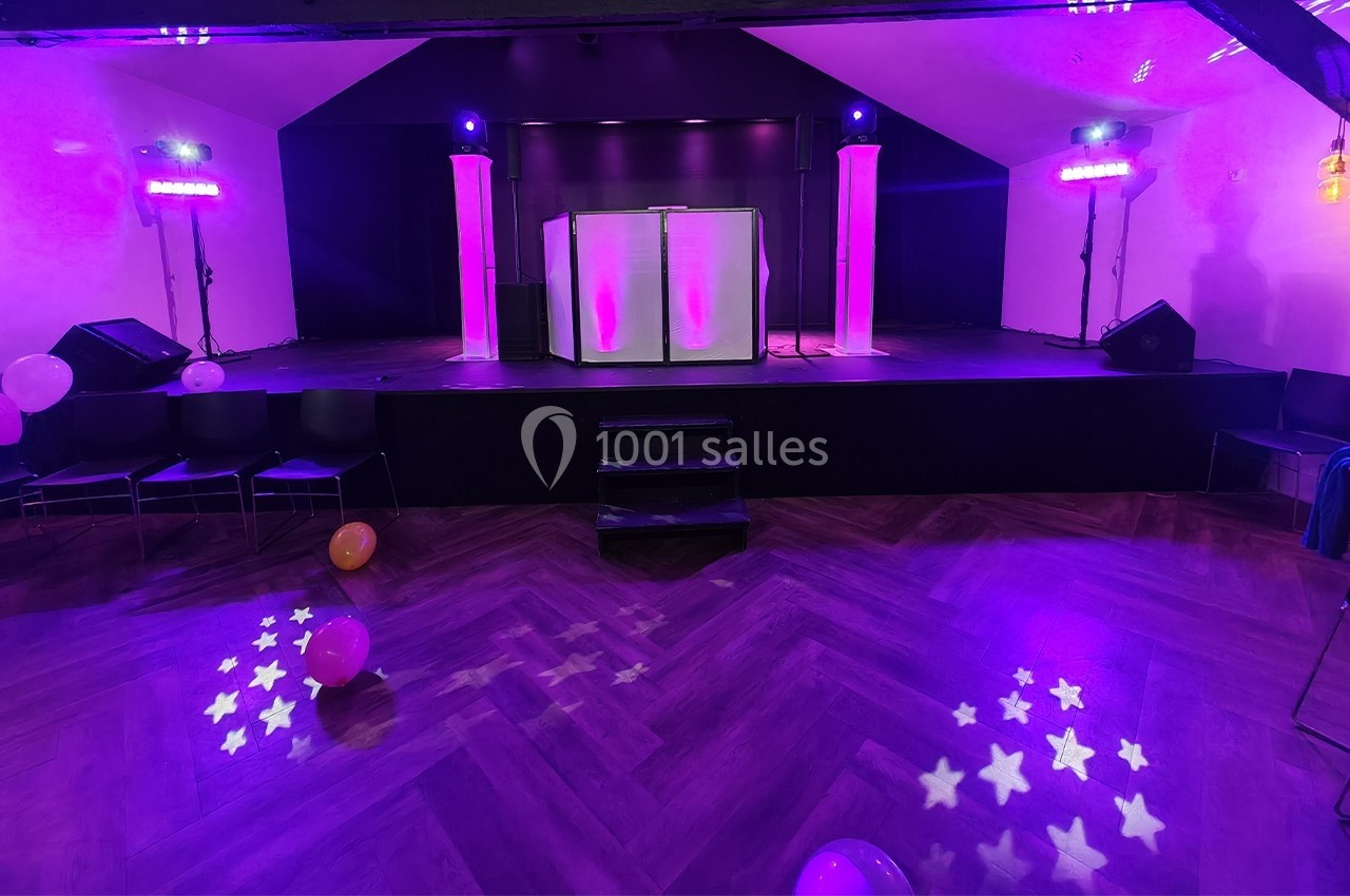 Scène éclairée de lumières violettes avec une piste de danse en parquet et des ballons au sol.