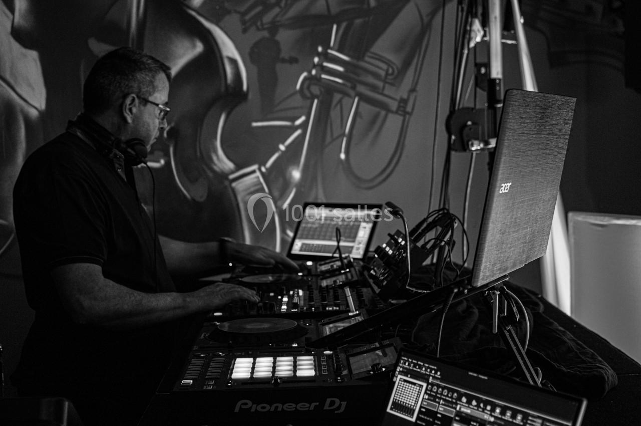 Un DJ mixe de la musique sur une table de mixage entourée d'équipements électroniques dans un studio sombre.