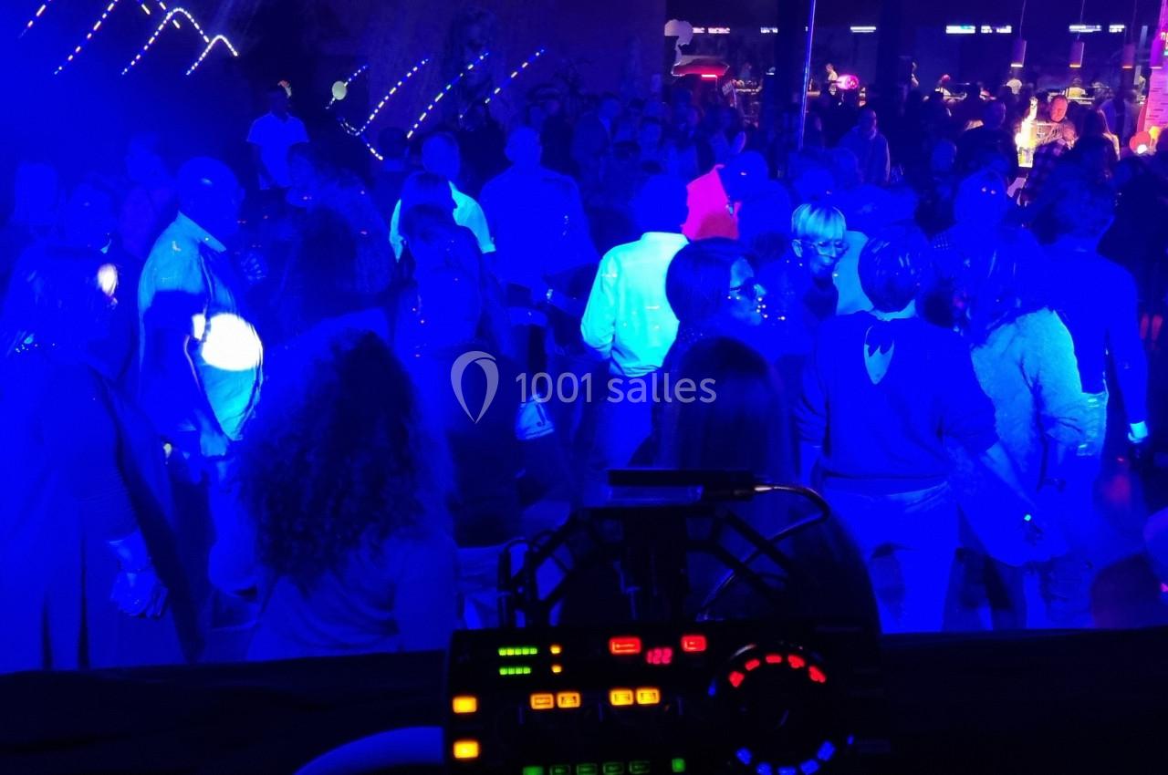 Foule dansante dans une ambiance lumineuse bleutée, vue depuis une table de mixage en arrière-plan.