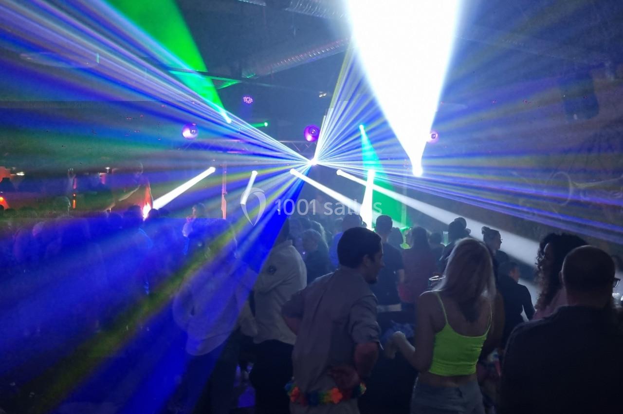 Des personnes dansent dans une salle sombre illuminée par des faisceaux lumineux colorés et des projecteurs.