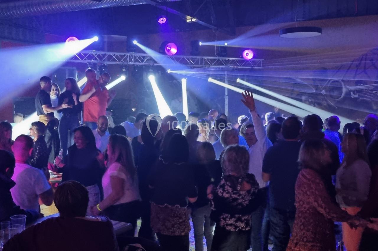 Groupe de personnes dans une salle animée avec éclairage coloré, musique en direct et ambiance festive.