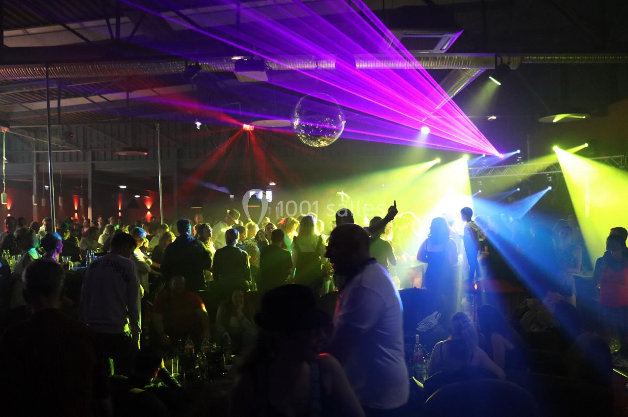 Foule dans une salle de concert avec des jeux de lumière colorés et une ambiance festive.