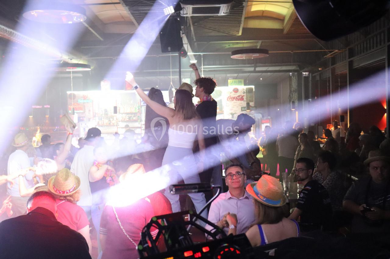 Personnes dansant et socialisant dans une ambiance festive avec éclairages lumineux dans un bar ou une discothèque.