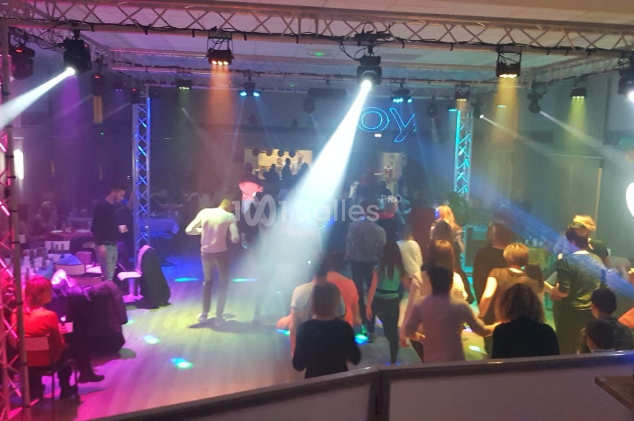 Des personnes dansent sur une piste éclairée par des jeux de lumière colorés dans une salle animée.