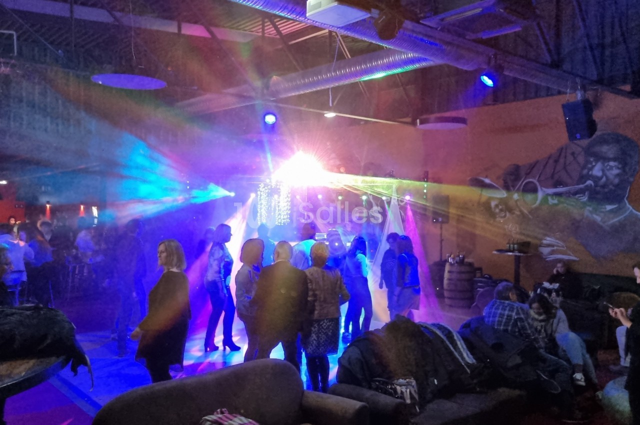 Groupe de personnes dans une salle animée avec jeux de lumière colorés et fresque murale représentant un musicien.