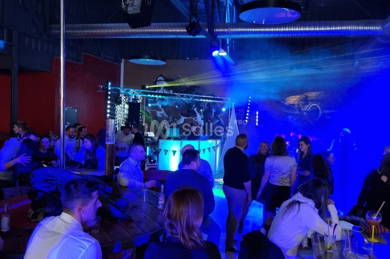 Des personnes dansent et discutent dans une salle avec éclairage coloré, musique et ambiance festive.