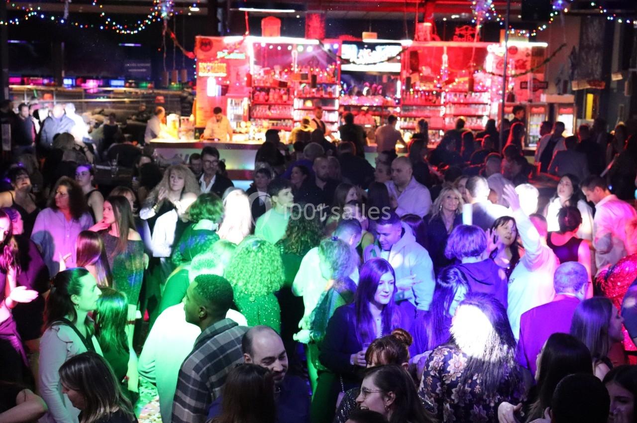 Foule dans une discothèque animée avec éclairages colorés et un bar illuminé en arrière-plan.