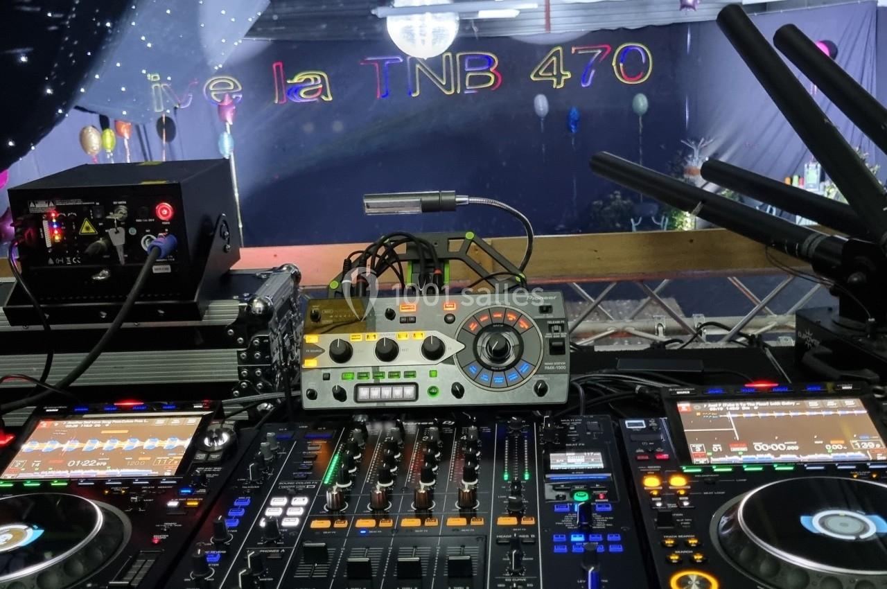 Vue d'une table de mixage DJ avec platines et équipements audio, éclairée dans une salle décorée pour un événement.