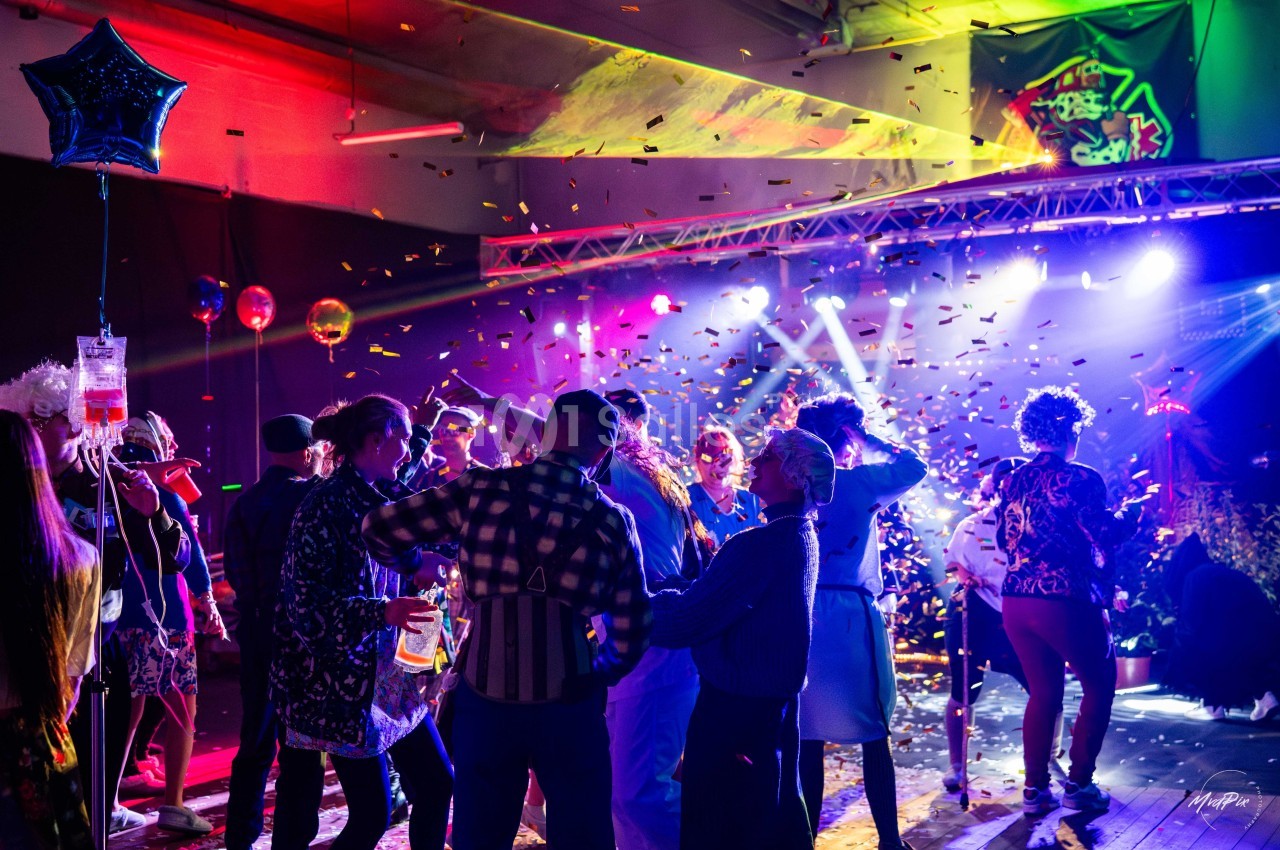 Personnes dansant sous des lumières colorées et des confettis dans une ambiance festive en intérieur.