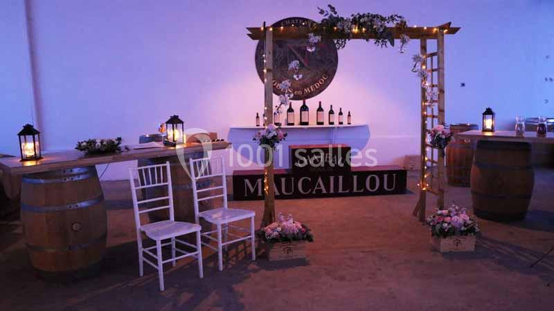 Décoration avec arche lumineuse, tonneaux, chaises et bouteilles de vin exposées dans une salle du Château Maucaillou.