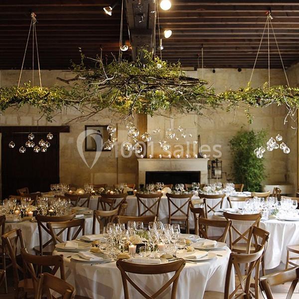 Salle de réception décorée avec des tables rondes dressées, des suspensions végétales et des lumières suspendues.