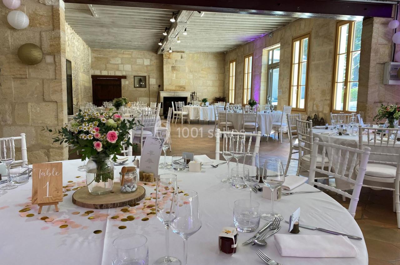 Salle de réception décorée avec des tables dressées, des fleurs et des éléments festifs dans un cadre en pierre.