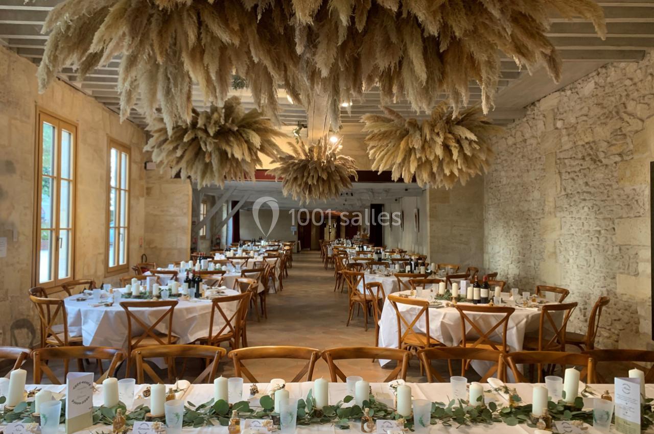 Salle de réception décorée avec des tables dressées, des chandelles et des suspensions de fleurs séchées au plafond.