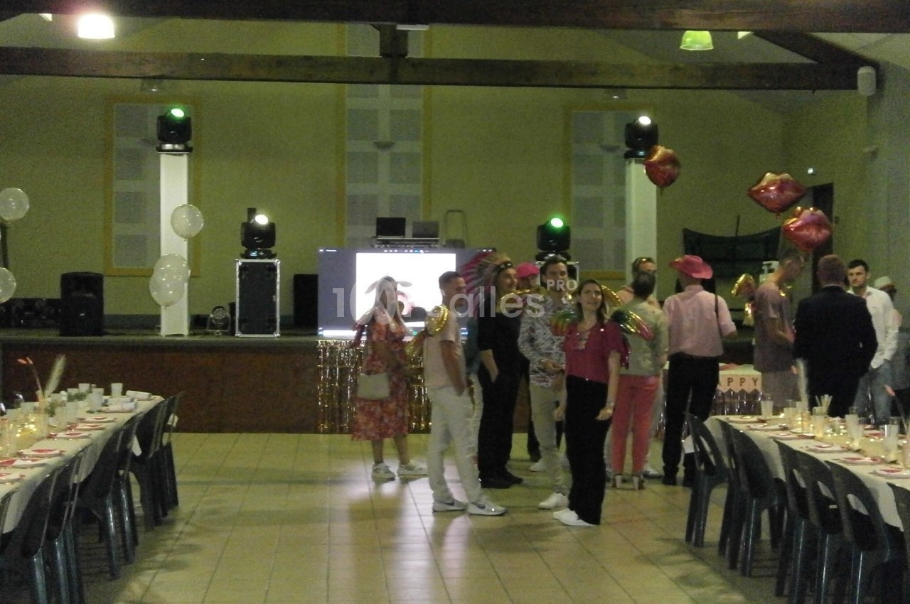 Des personnes déguisées discutent dans une salle décorée pour une fête, avec tables dressées et scène en arrière-plan.
