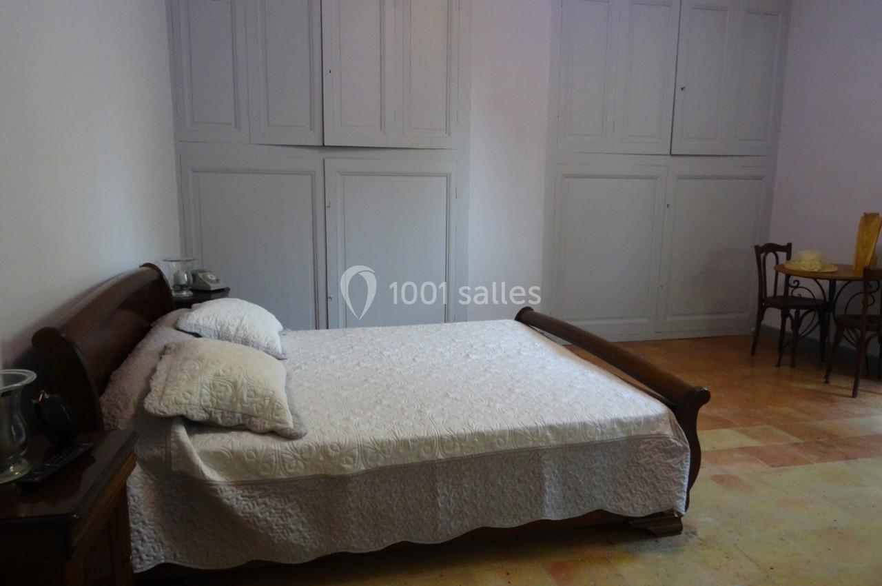 Chambre avec un lit double en bois, draps blancs, armoires encastrées et table avec chaises dans un coin.