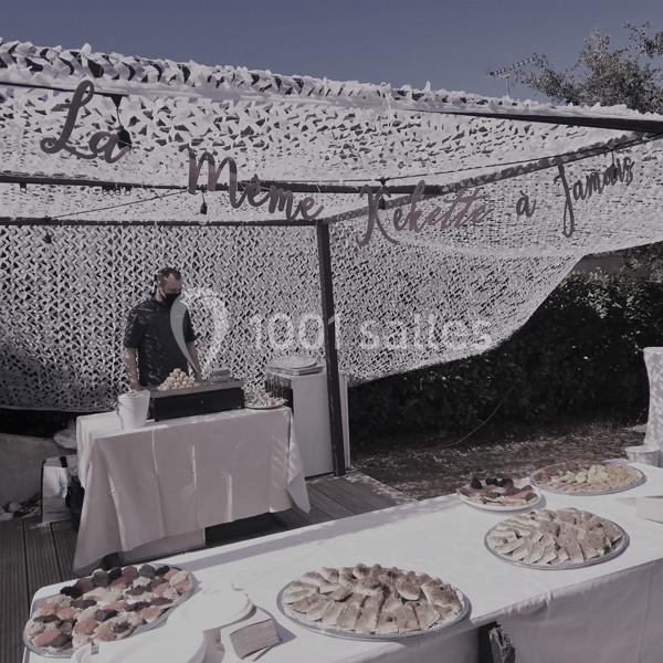 Stand de restauration en extérieur avec un homme derrière un comptoir, des tables garnies de plats variés au premier plan.