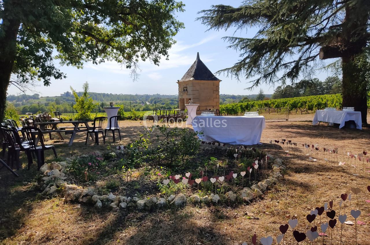 Espace extérieur avec tables et décorations, entouré de vignes et d'arbres, devant une petite bâtisse en pierre.