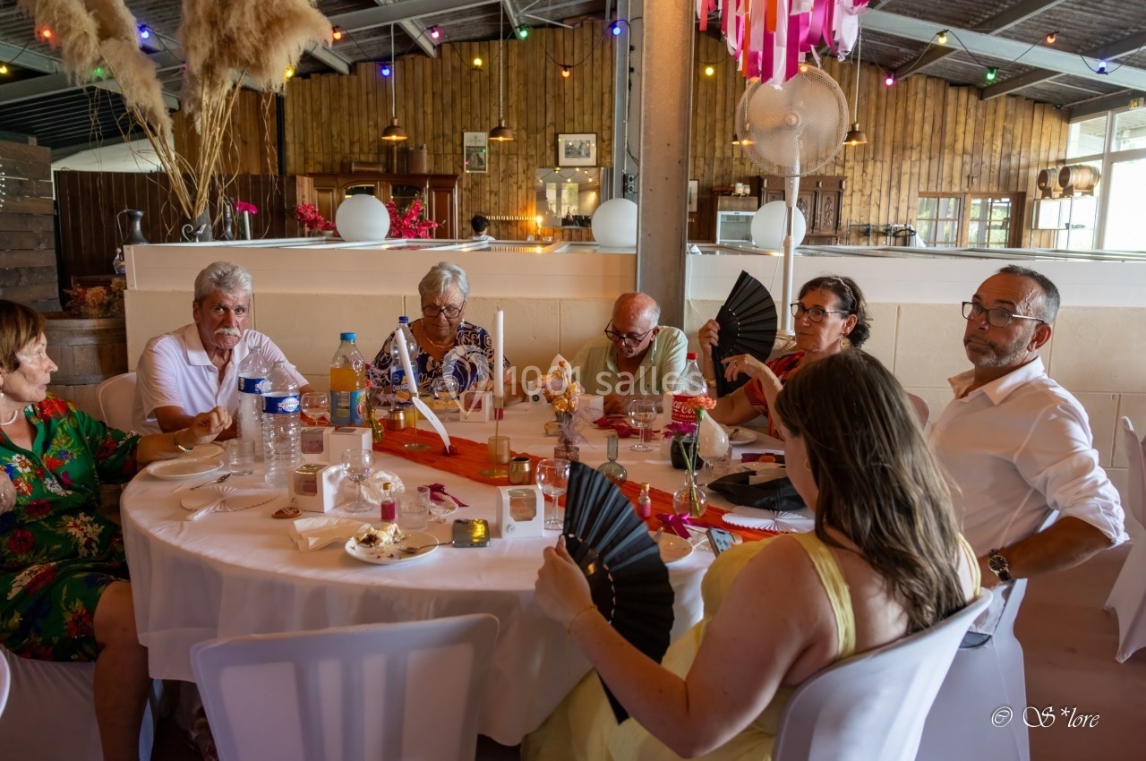 Des personnes assises autour d'une table décorée, partageant un repas dans une salle festive avec des lumières colorées.