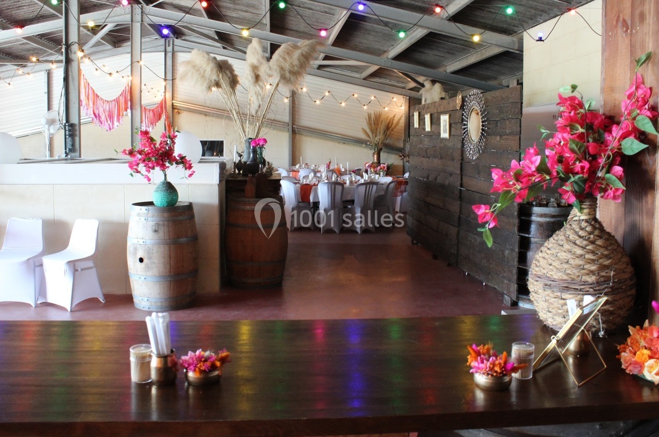 Salle décorée pour un événement avec tables dressées, guirlandes lumineuses colorées et arrangements floraux.