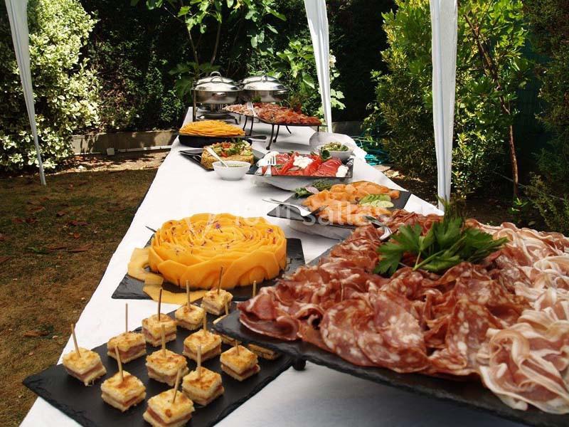Buffet en plein air avec charcuterie, fruits, légumes, amuse-bouches et plats variés disposés sur une table blanche.