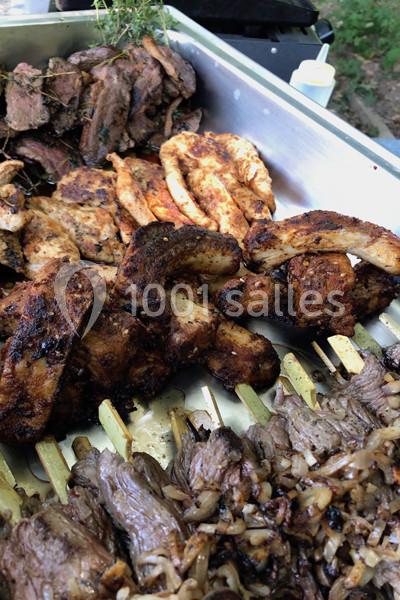 Viandes grillées variées, dont brochettes et morceaux marinés, présentées sur un plateau en extérieur.