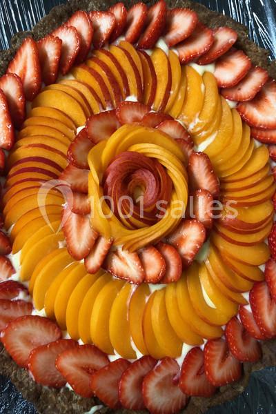 Tarte garnie de tranches de fraises et d'abricots disposées en spirale sur une crème claire.
