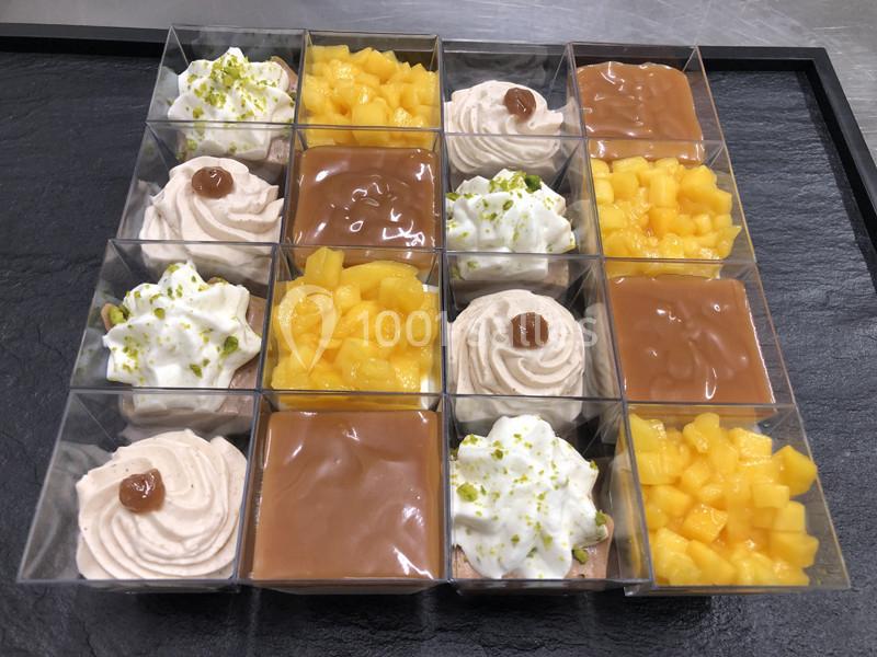 Assortiment de verrines sucrées avec mousse, caramel, mangue et chantilly, disposées sur un plateau noir.
