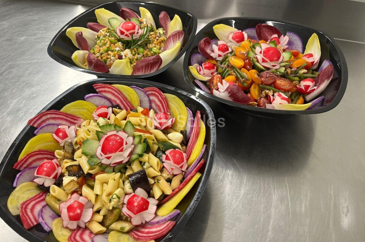 Trois salades colorées présentées dans des bols noirs, composées de légumes variés et décorées de radis sculptés.