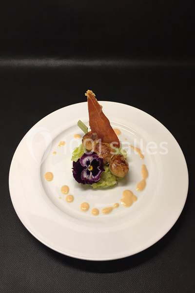 Assiette gastronomique avec noix de Saint-Jacques, purée verte, fleur comestible et décorations de sauce.