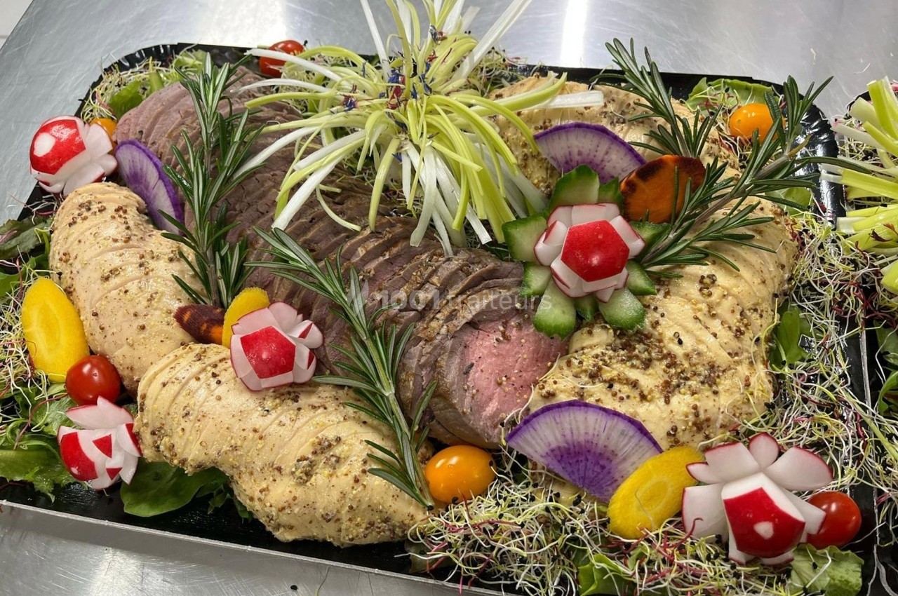 Plateau de viandes tranchées garnies d'herbes, légumes décoratifs et pousses, présenté sur un lit de salade.