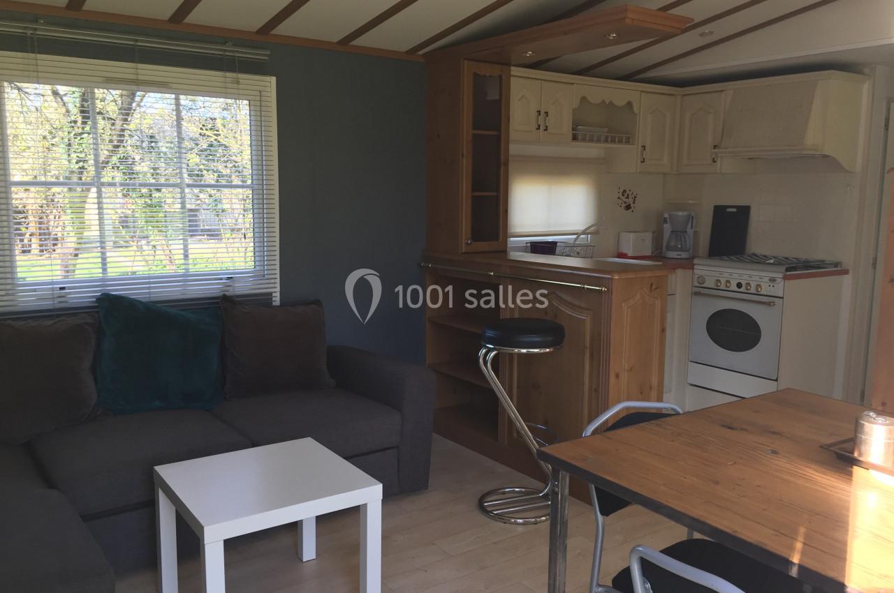 Intérieur d'un mobil-home avec salon, canapé, table basse, cuisine équipée et table à manger en bois.