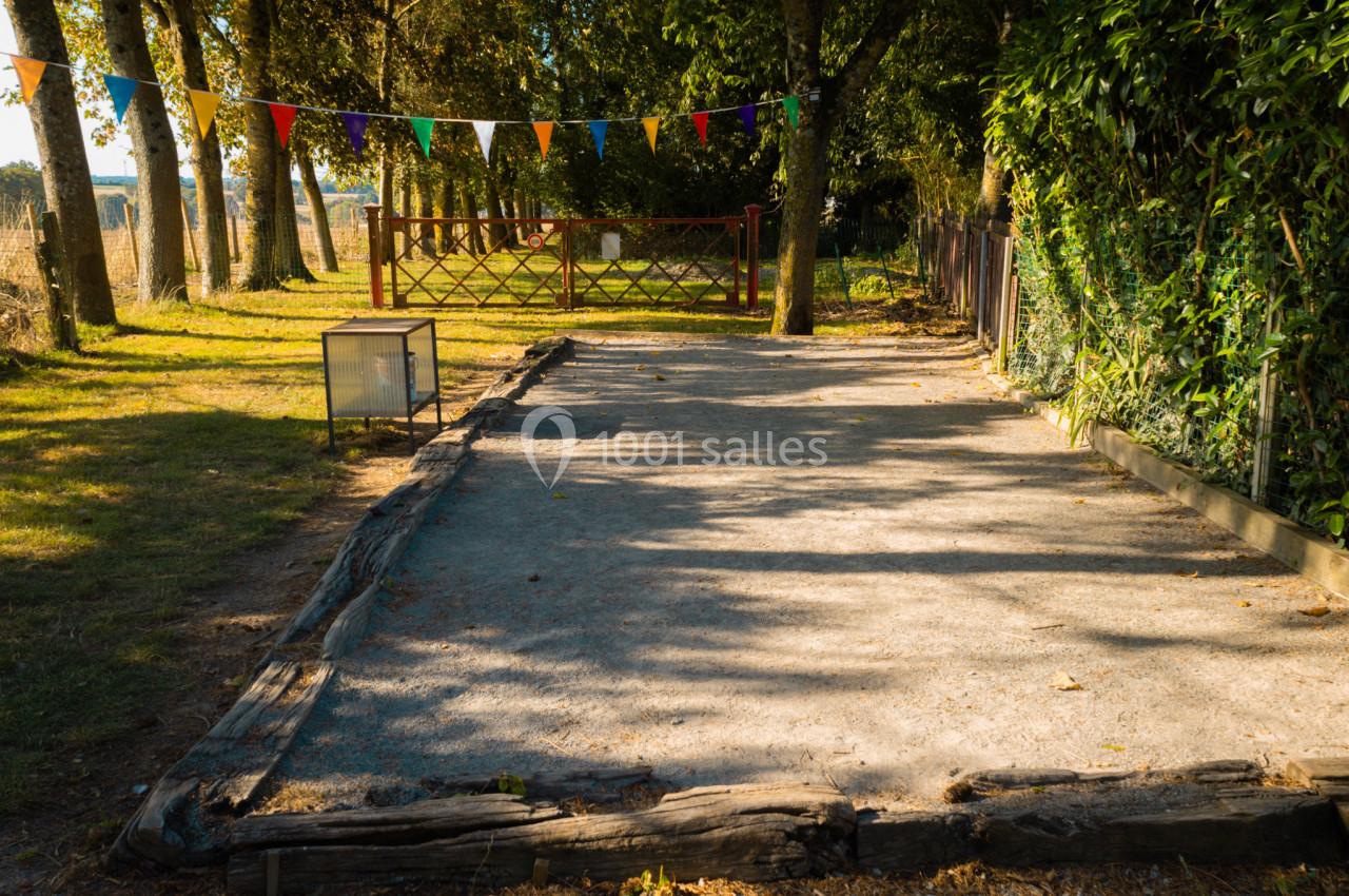 Terrain de pétanque ombragé entouré d'arbres, avec des fanions colorés suspendus en arrière-plan.