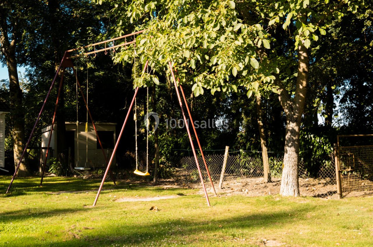 Portique avec balançoires dans un jardin ensoleillé, entouré d'arbres et de clôtures.