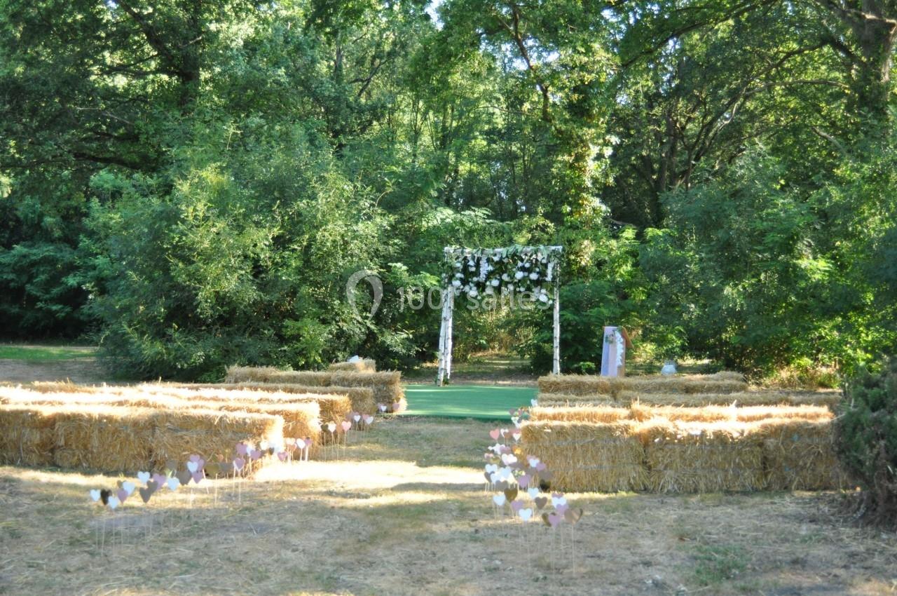 Allée centrale bordée de bottes de paille menant à une arche fleurie dans un cadre naturel verdoyant.