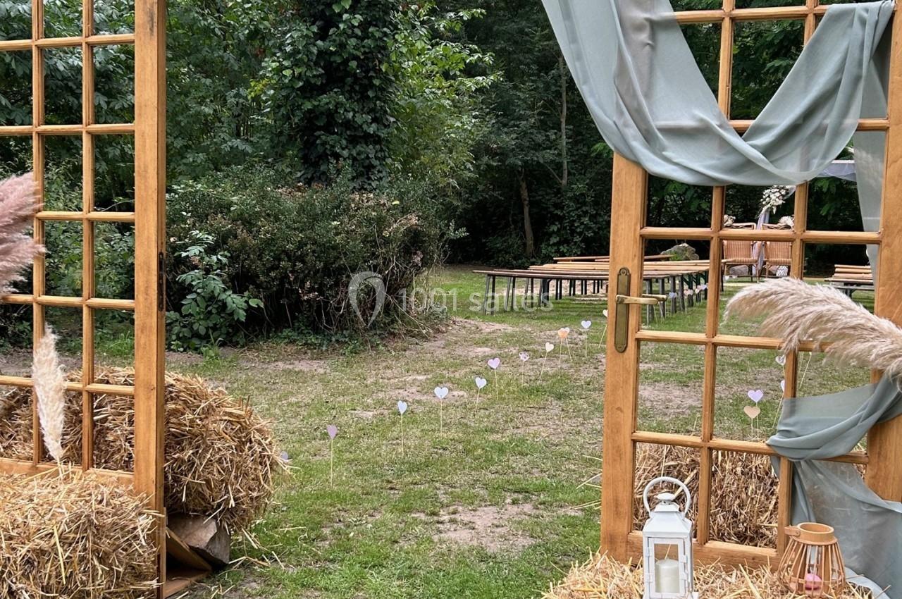 Entrée décorative en bois avec rideaux et bottes de paille, donnant sur un espace extérieur aménagé pour un événement.